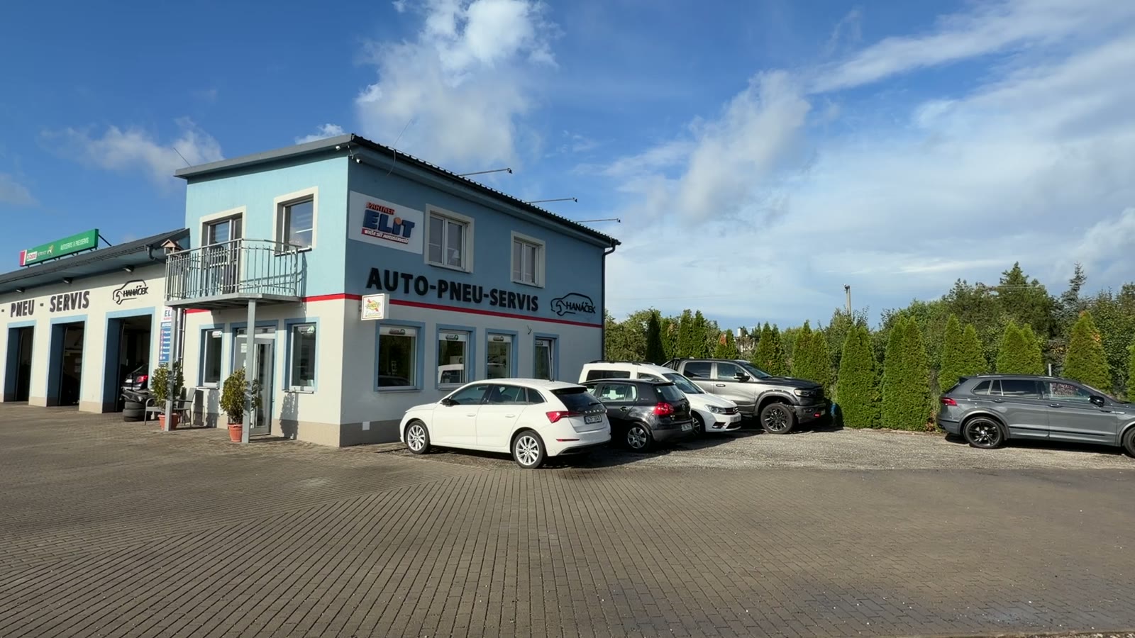 Dílna Hanáček Auto — budova autoservisu s nápisem AUTO-PNEU-SERVIS a parkovištěm